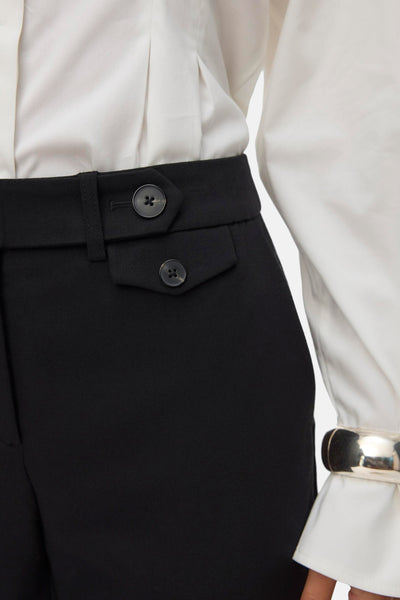 Pantalon noir de Vero Moda avec une ceinture à bouton, porté avec une chemise blanche et un bracelet argenté.

