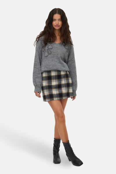 Geruite korte rok van VERO MODA, met meerkleurig Schots ruitpatroon en gedragen met een grijze trui en zwarte laarzen.