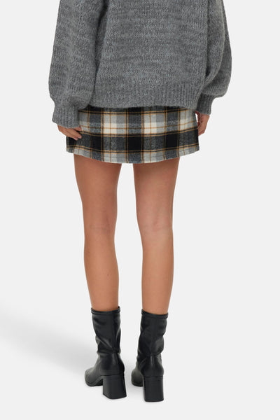 Geruit korte rok van VERO MODA®, gedragen met een grijze trui en zwarte laarzen.