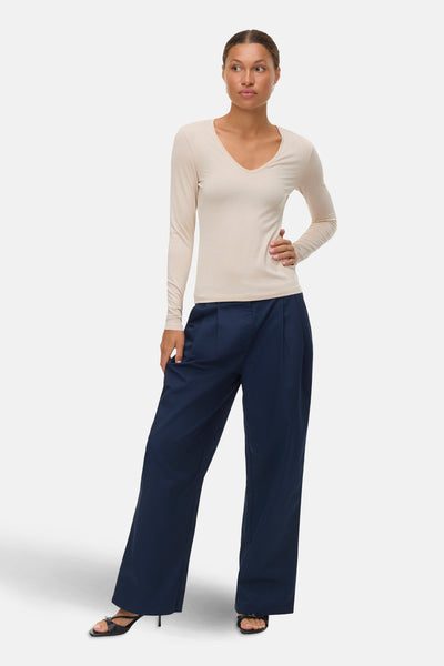 Beige blouse met lange mouwen van VERO MODA, gedragen met een marineblauwe broek en zwarte sandalen.