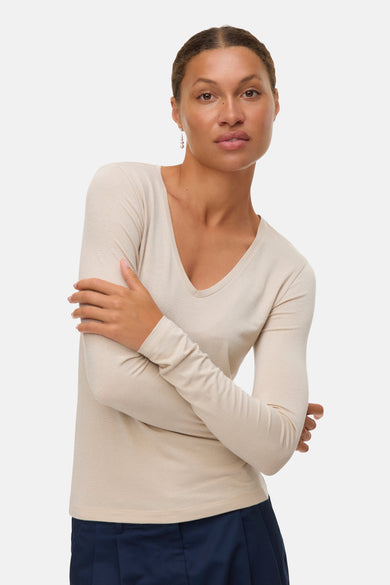 Beige blouse met lange mouwen van VERO MODA®, gedragen met een marineblauwe broek en lange oorbellen.