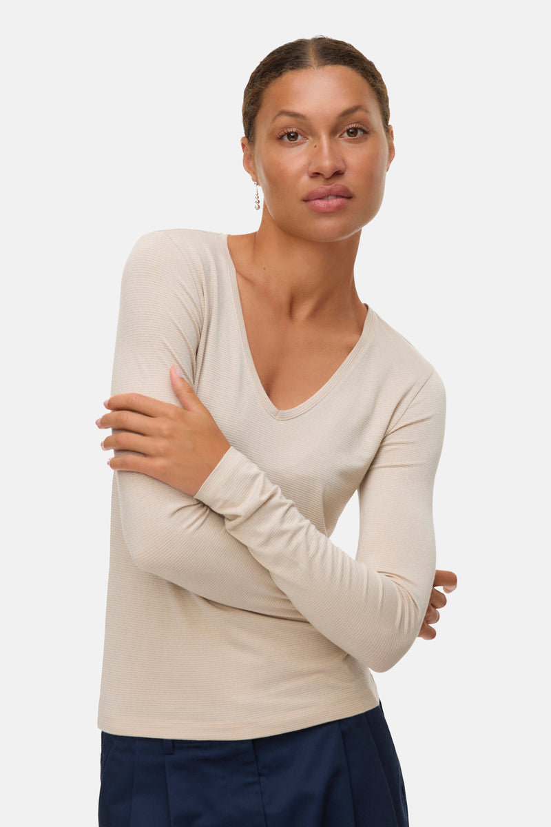 Beige blouse met lange mouwen van VERO MODA®, gedragen met een marineblauwe broek en lange oorbellen.