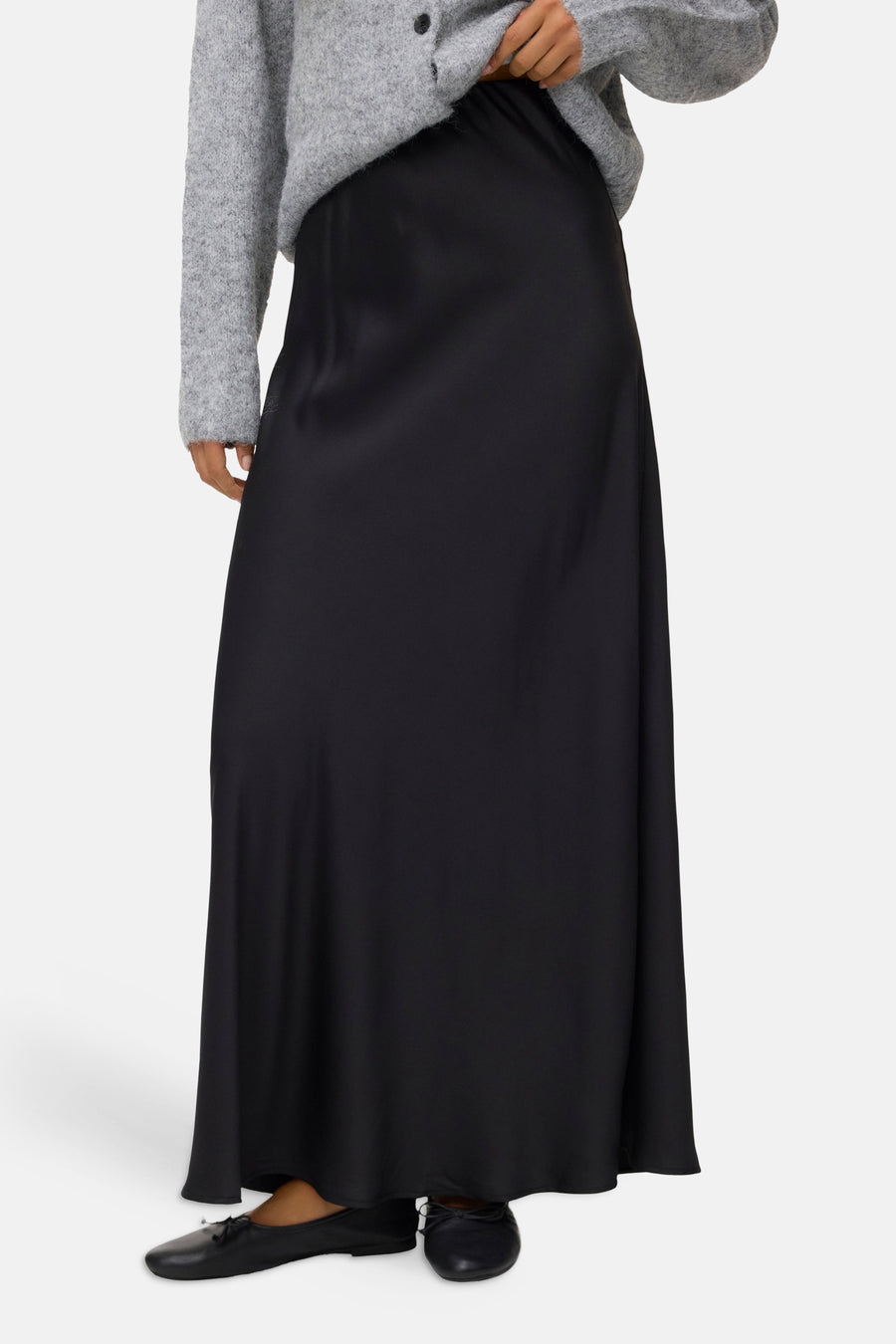 Black long flowing skirt with smooth satin-like texture, worn with gray sweater and black flat shoes, front view