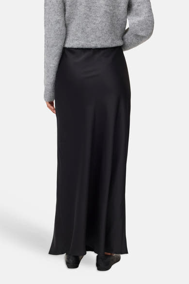 Black long skirt with smooth satin finish, back view, worn with gray sweater and black shoes