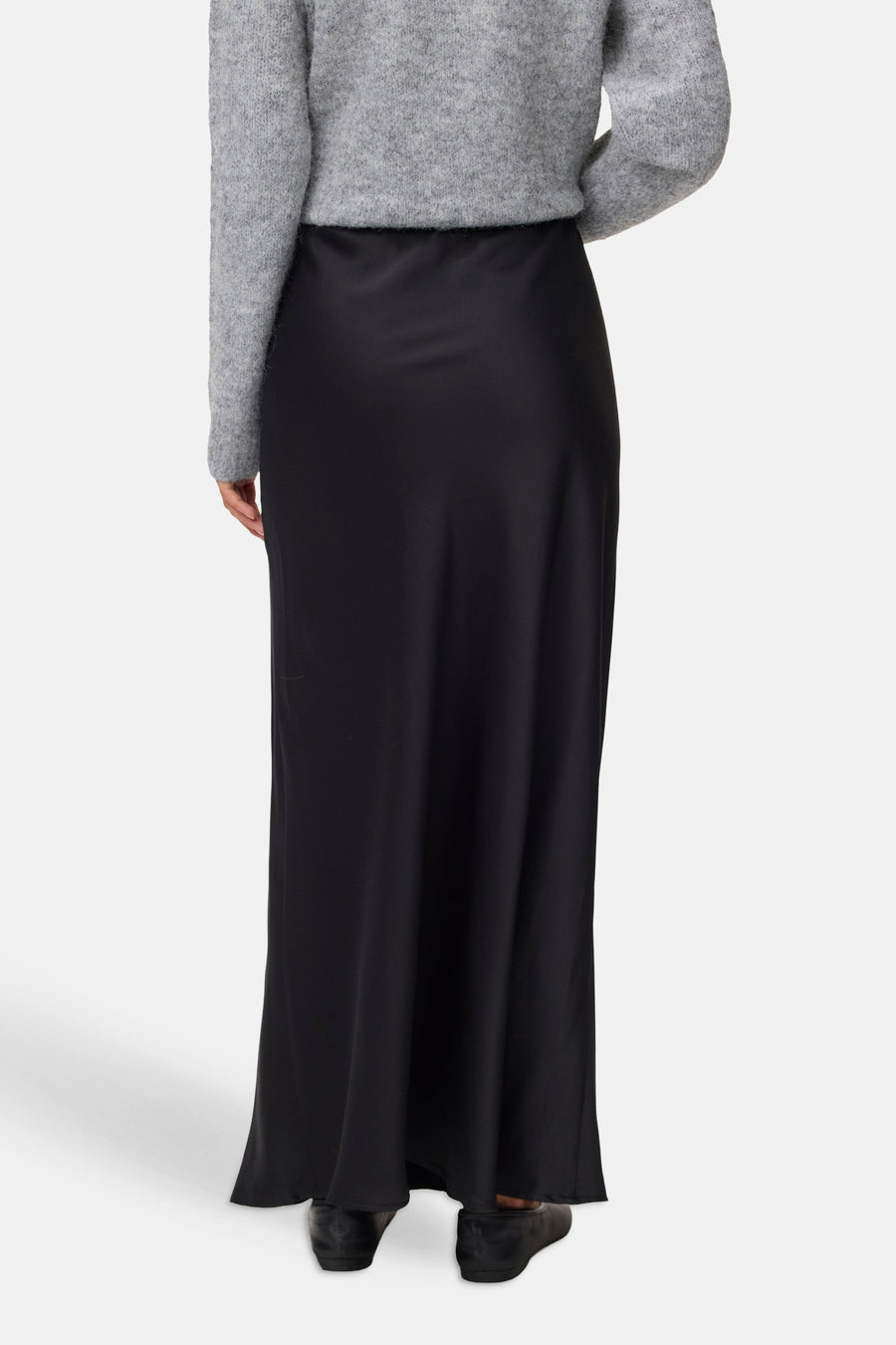 Black long skirt with smooth satin finish, back view, worn with gray sweater and black shoes