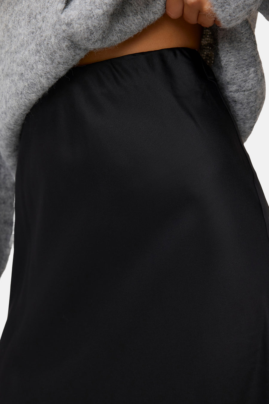 Black long skirt with smooth satin texture, worn with gray fuzzy sweater, close-up front view