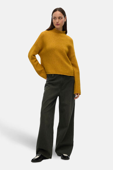 Gele coltrui van VERO MODA®, gedragen met een wijde zwarte broek en lakleren schoenen.