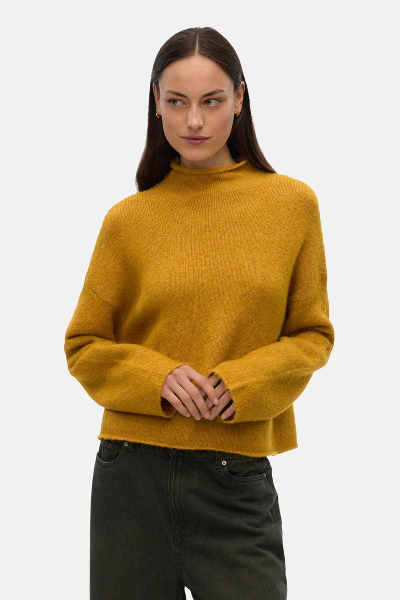 Gele coltrui van VERO MODA, gedragen met een effen donkergroene jeans en kleine gouden oorbellen.
