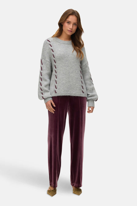 Grijze trui met ronde hals van Vero Moda, met decoratieve details op de mouwen en gedragen met een fluwelen broek.