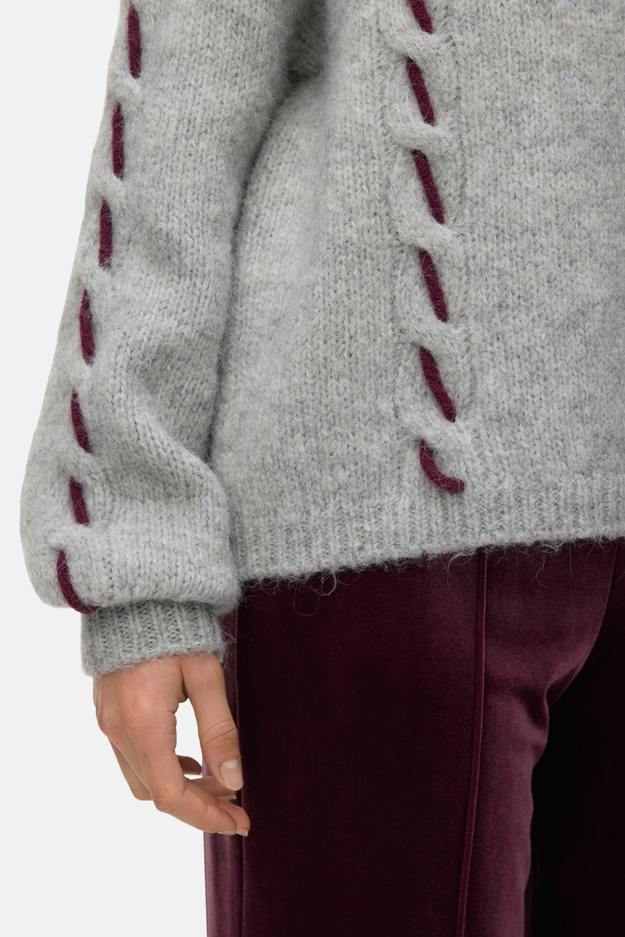 Grijze rondehals trui van VERO MODA, met bordeaux gevlochten details op de mouwen, gedragen met een bordeaux fluwelen broek.