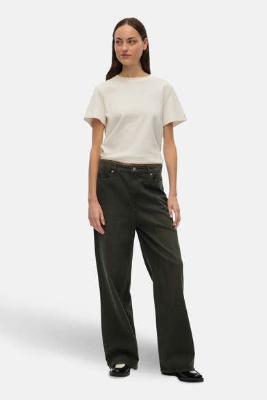 Gekleurde groene jeans van VERO MODA, losse pasvorm en wijde pijpen, gedragen met een gebroken wit T-shirt en zwarte lakleren schoenen.
