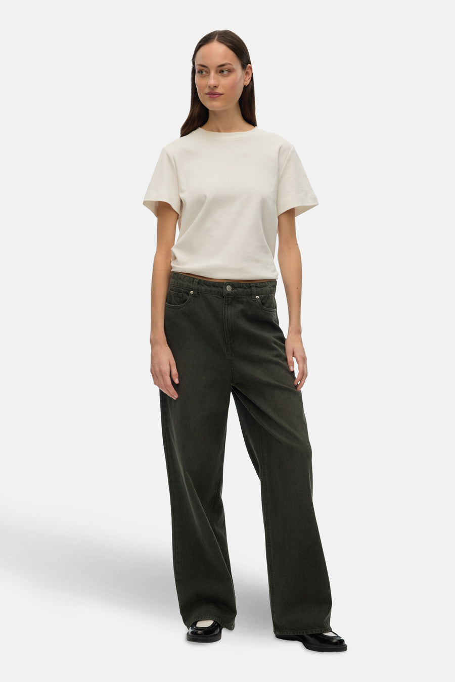 Gekleurde groene jeans van VERO MODA, losse pasvorm en wijde pijpen, gedragen met een gebroken wit T-shirt en zwarte lakleren schoenen.