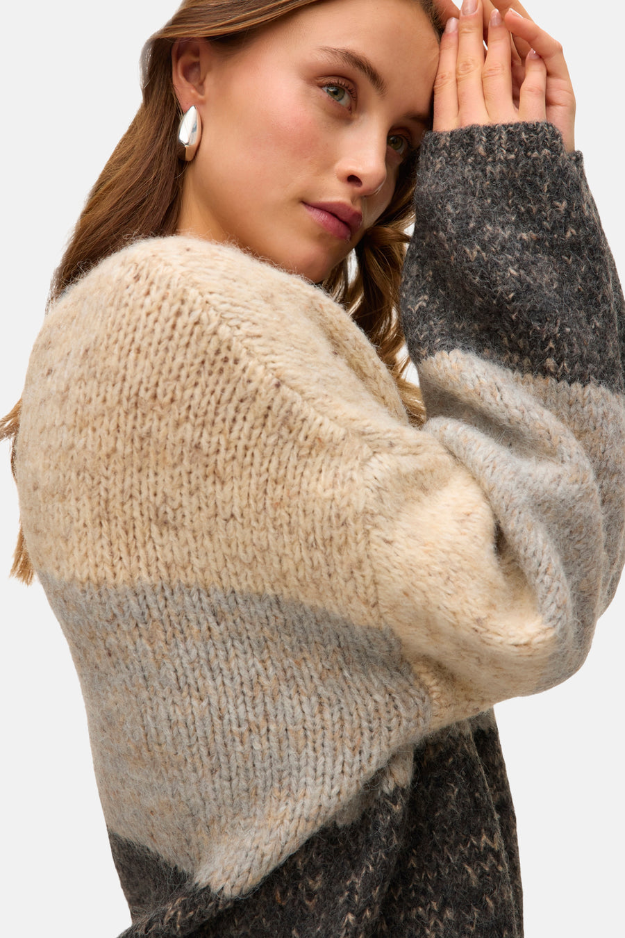 Beige ronde hals trui van VERO MODA® in dik gestreept breiwerk, gedragen met zilveren oorbellen.