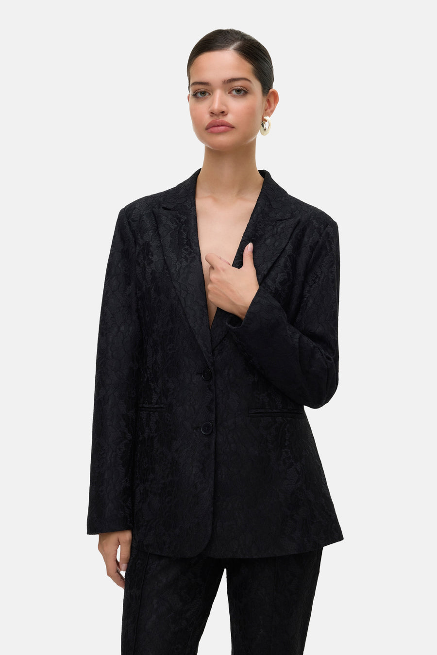 Zwarte blazer van VERO MODA met textuurpatroon, open gedragen met een hand in de zak.