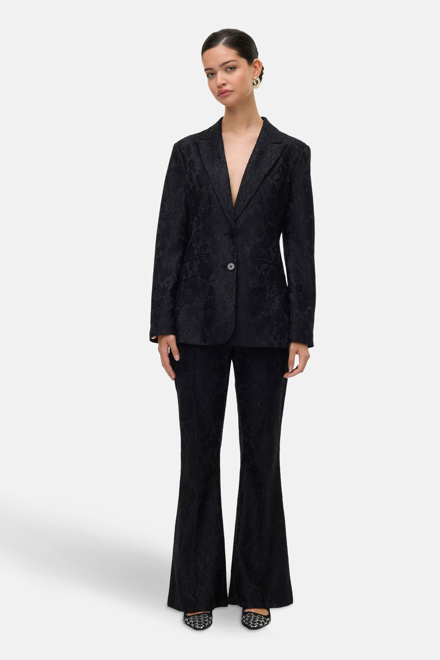 Zwarte broek van VERO MODA® met toon-op-toon bloemenpatroon, uitlopende pijpen en glitter schoenen.