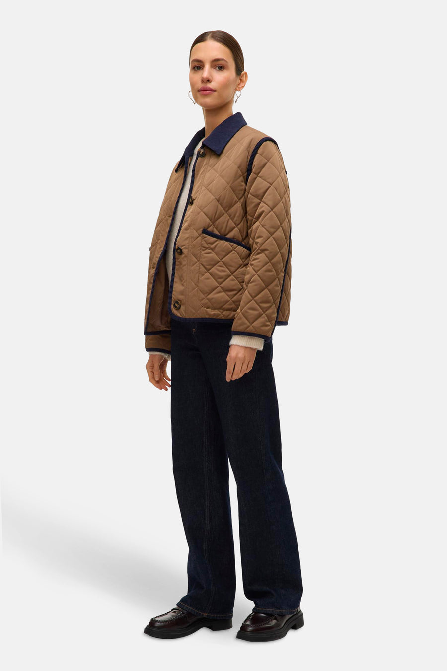 Veste courte marron de VERO MODA, avec motif matelassé et finitions marine, portée sur un pull clair et un jean bleu foncé.