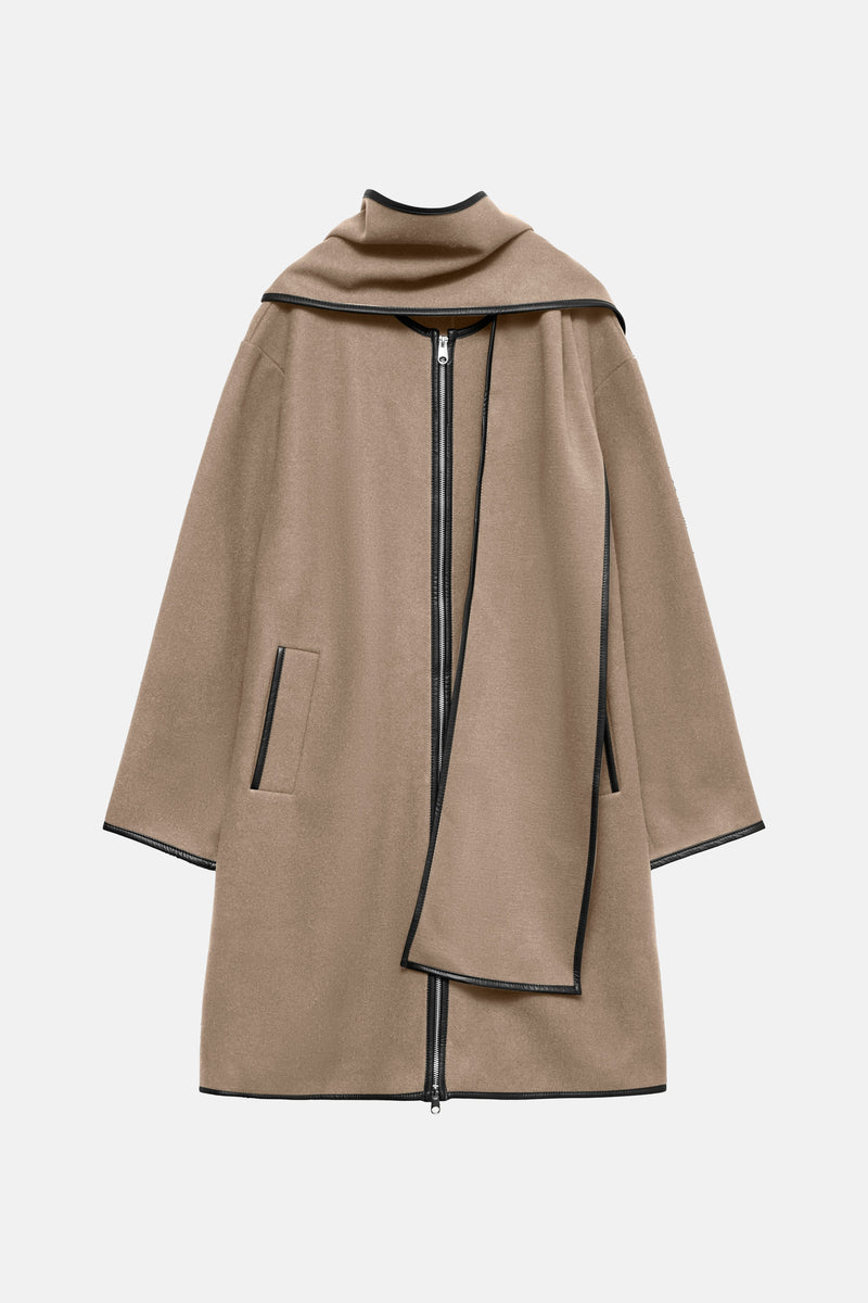 Lange beige jas van VERO MODA met ritssluiting aan de voorkant en zwarte afwerkingen.