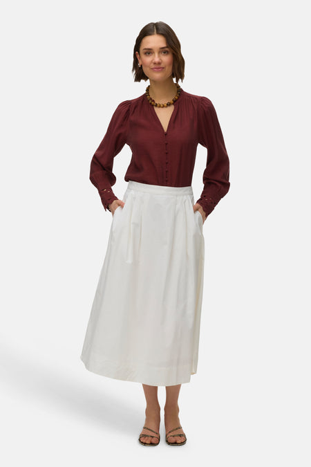 Chemisier brique à manches longues de VERO MODA, avec une jupe blanche longue et un collier de perles.