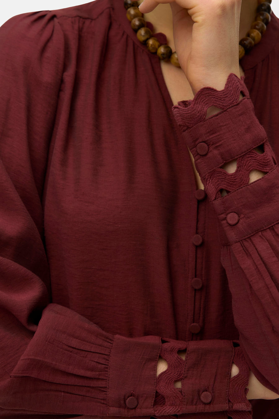 Baksteenrode blouse met lange mouwen van VERO MODA, versierd met knopen, kanten manchetten en een ronde hals met kralenketting.