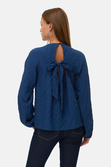 Blouse bleu à manches longues de Vero Moda, avec nœud décoratif à l'arrière et texture froissée.