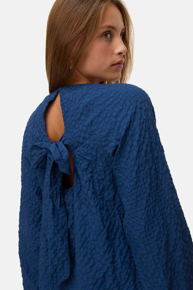 Chemisier bleu à manches longues de VERO MODA®, avec un nœud décoratif à l'arrière et une texture gaufrée.