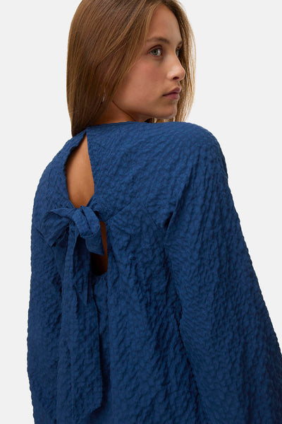 Chemisier bleu à manches longues de VERO MODA®, avec un nœud décoratif à l'arrière et une texture gaufrée.