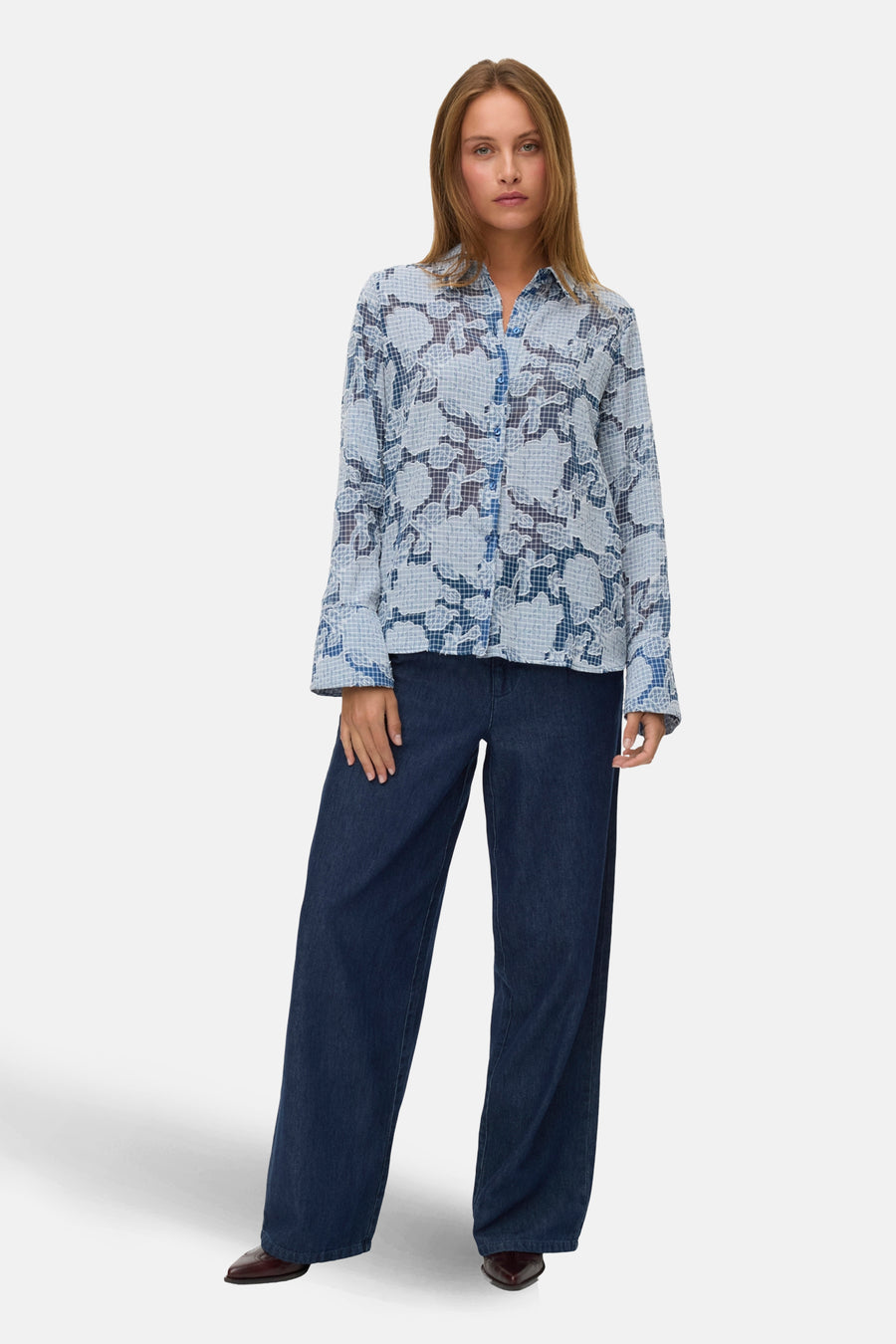 Chemisier bleu à manches longues de VERO MODA® avec motif floral et carreaux, porté avec un jean large et des bottines.