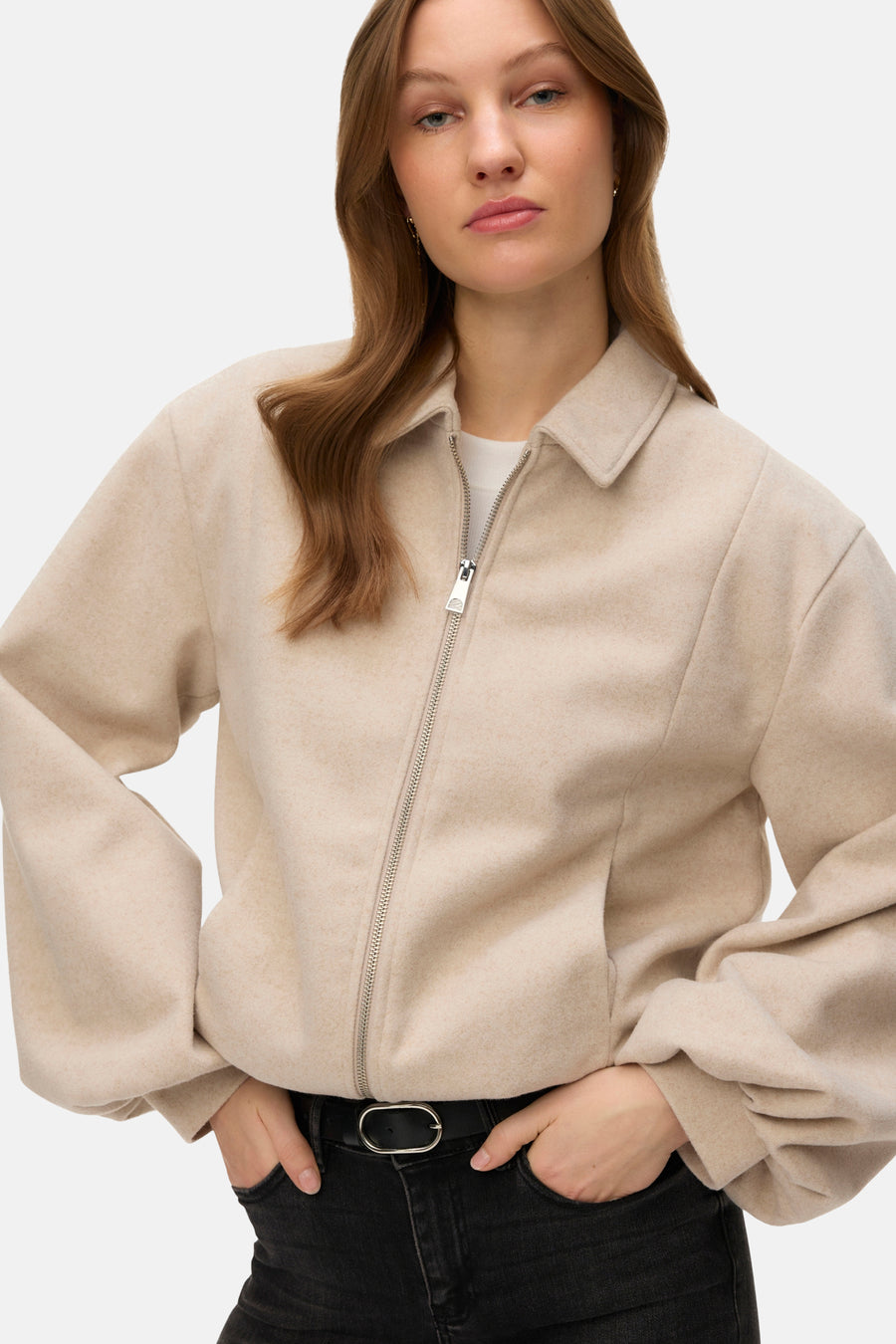 Veste courte écru de VERO MODA, avec fermeture éclair et portée sur un jean noir ceinturé.
