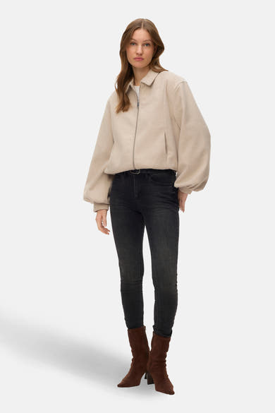 Veste courte écru de VERO MODA, avec une fermeture éclair argentée, portée avec un jean noir et des bottes en daim marron.