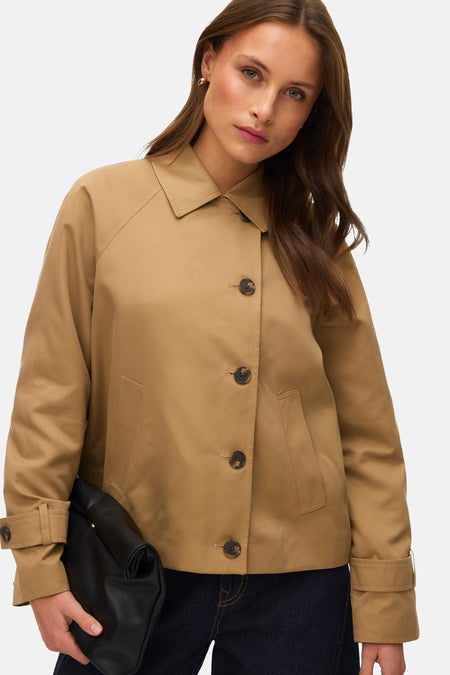 Veste courte beige de VERO MODA, avec boutons marron, poches et tenant une pochette noire.