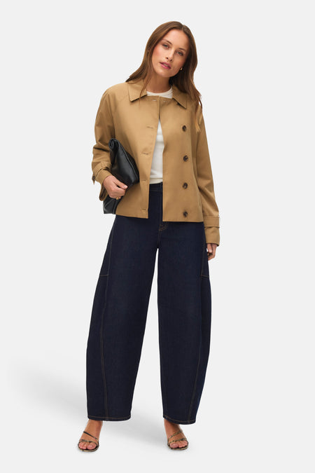Veste courte beige de VERO MODA, avec boutons marron, portée avec un t-shirt blanc, un pantalon large bleu marine et une pochette noire.
