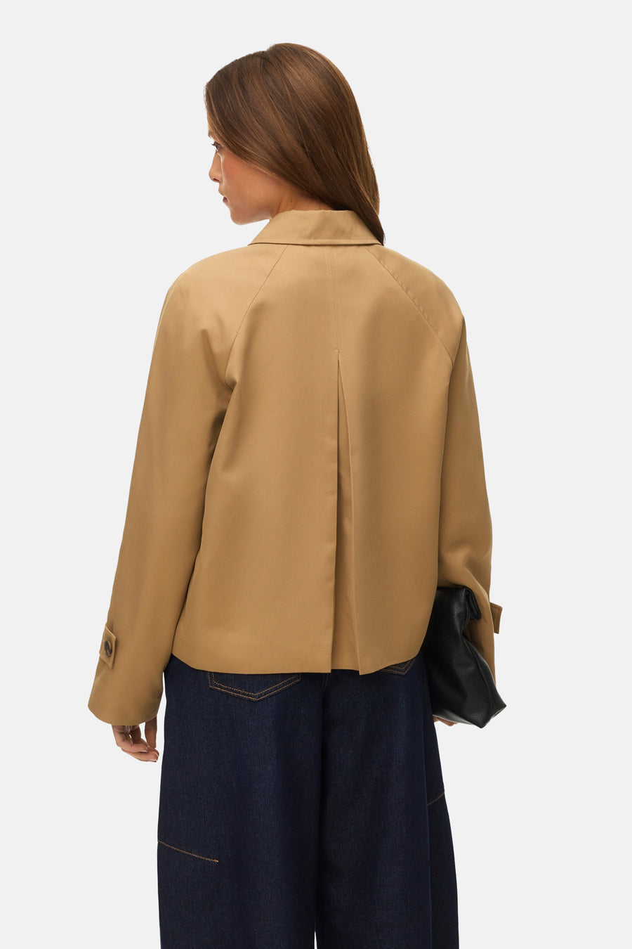 Veste courte beige de VERO MODA®, avec une pliure au dos, portée avec un pantalon en jean foncé et une pochette noire.
