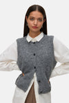 Débardeur gris en tricot par Vero Moda, porté sur une chemise blanche à manches longues avec des boucles d'oreilles pendantes.