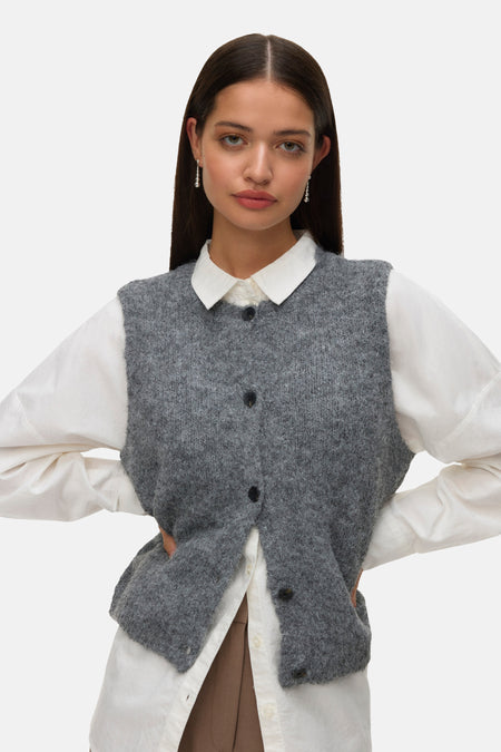 Débardeur gris en tricot par Vero Moda, porté sur une chemise blanche à manches longues avec des boucles d'oreilles pendantes.