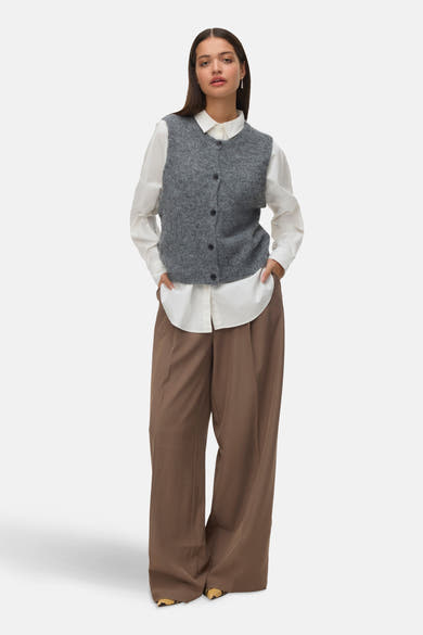 Débardeur gris en tricot de VERO MODA®, porté sur une chemise blanche avec un pantalon ample marron.