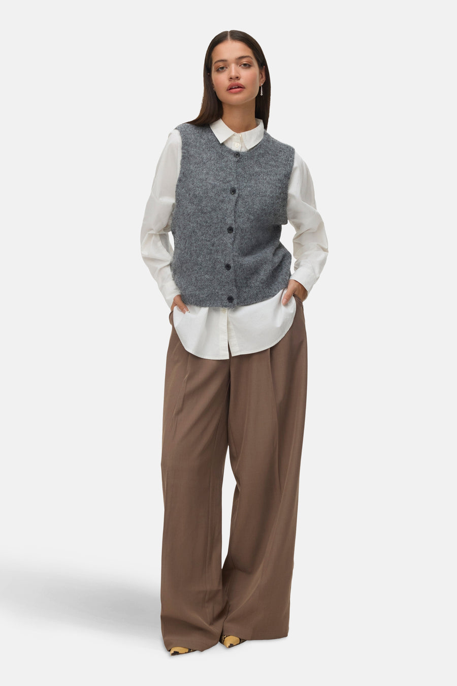 Débardeur gris en tricot de VERO MODA®, porté sur une chemise blanche avec un pantalon ample marron.