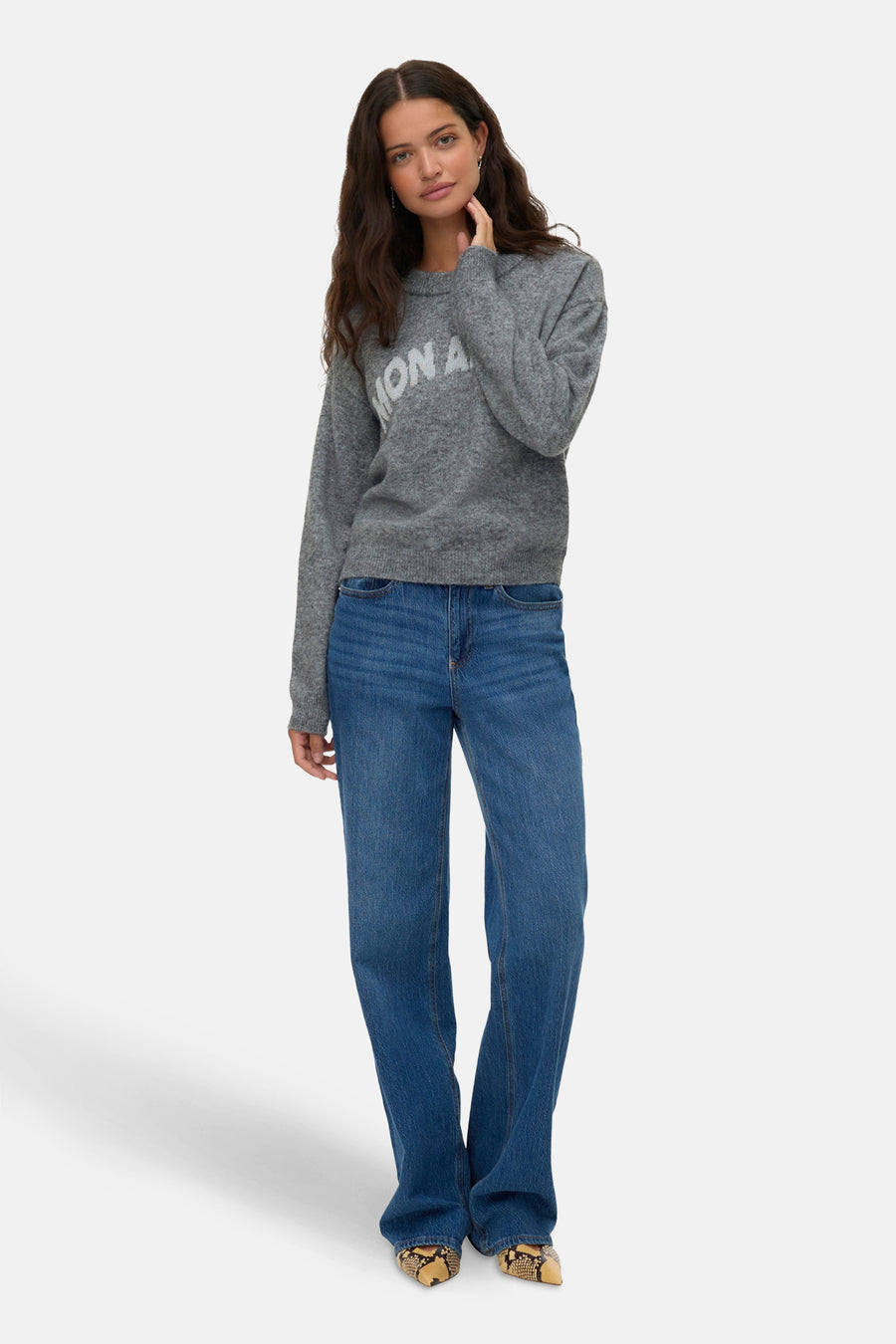 Grijze rondehals trui van VERO MODA, met witte opdruk, gedragen met een wijde blauwe jeans en slangenprint pumps.