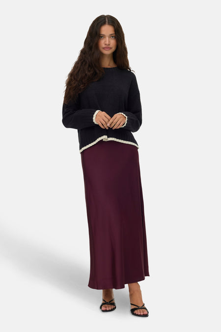 Pull à col rond noir de VERO MODA, orné de bordures contrastantes aux poignets et à l'ourlet, porté avec une jupe longue bordeaux.
