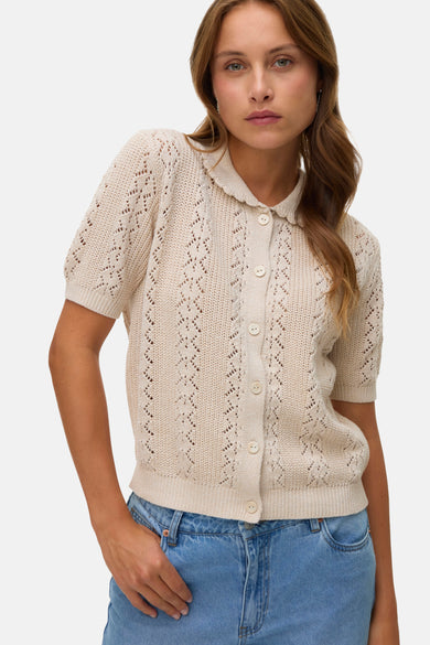 Gilet beige à boutons de VERO MODA, avec motifs ajourés et col classique, porté sur un jean bleu.
