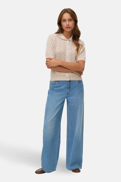 Gilet beige de VERO MODA, avec motif ajouré et col à revers, porté avec un jean ample.
