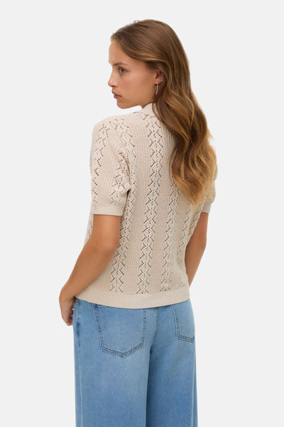 Gilet beige en tricot de VERO MODA, avec un motif ajouré et porté avec un jean ample.
