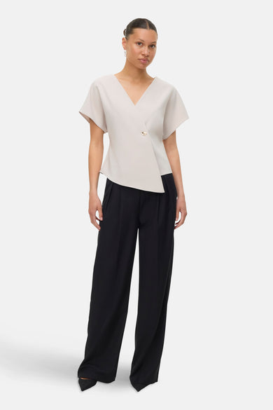 Ecru blouse met korte mouwen van VERO MODA, met een asymmetrische gouden knoop en een zwarte wijde broek.
