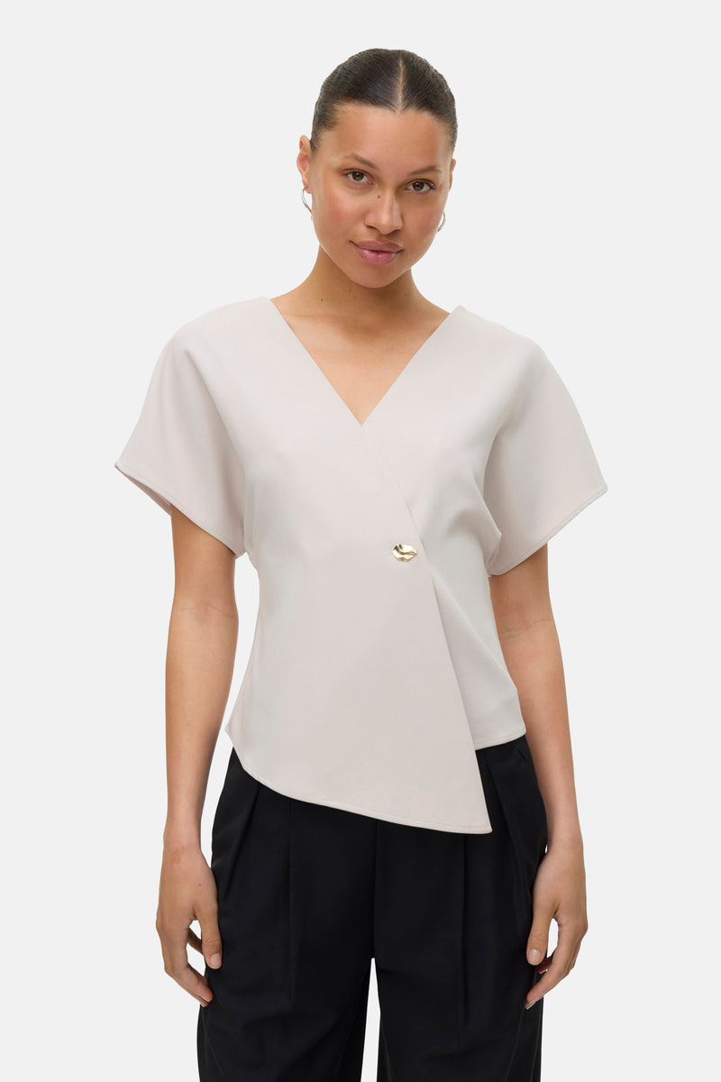 Ecru blouse met korte mouwen van VERO MODA, met gouden knoopsluiting en zwarte broek.