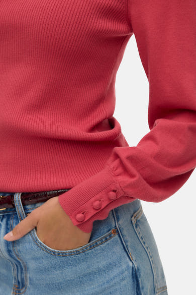 Pull à col rond rose de VERO MODA, côtelé avec manches longues boutonnées, porté avec un jean et une ceinture marron.