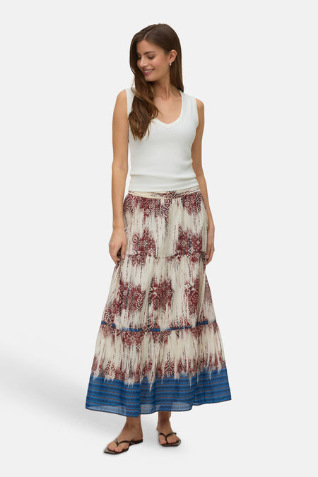 Jupe longue multicolore de VERO MODA® à motifs géométriques rouges et bleus, ourlet à bande bleue, portée avec un débardeur blanc.