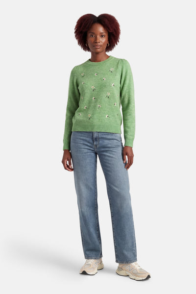 Groene trui met ronde hals van VERO MODA® met geborduurde bloemenpatronen op de voorkant, gedragen met een blauwe jeans en sneakers.