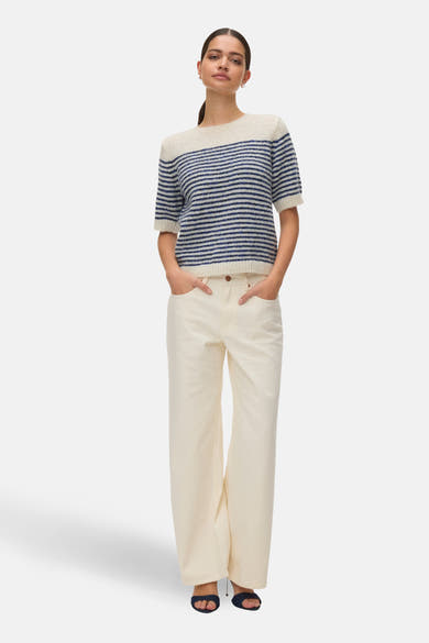 Pull à col rond bleu rayé de VERO MODA, porté avec un pantalon blanc et des sandales bleu foncé.