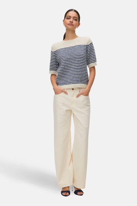 Pull à col rond bleu rayé de VERO MODA, porté avec un pantalon blanc et des sandales bleu foncé.