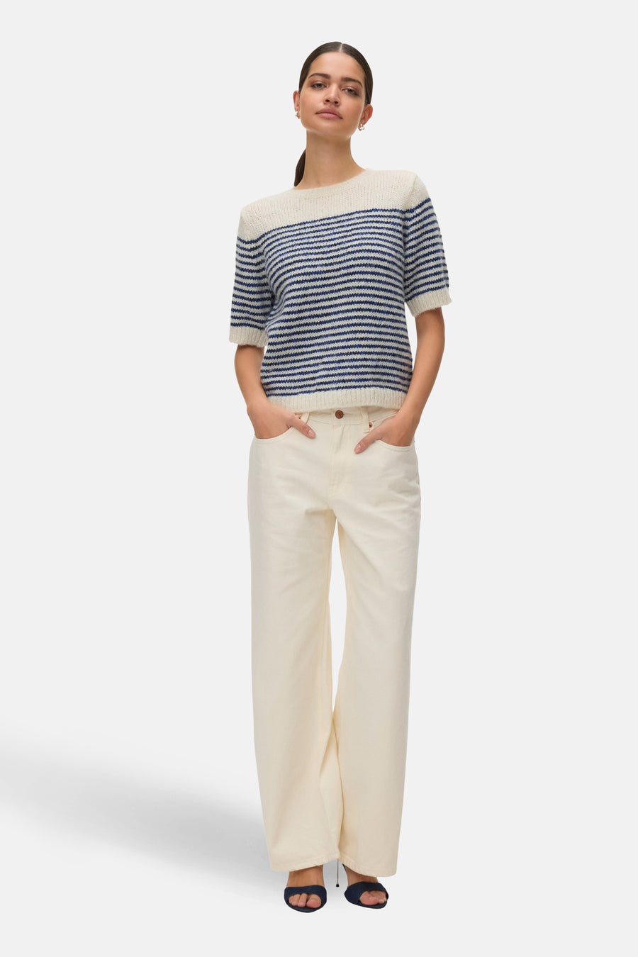 Pull à col rond bleu rayé de VERO MODA, porté avec un pantalon blanc et des sandales bleu foncé.