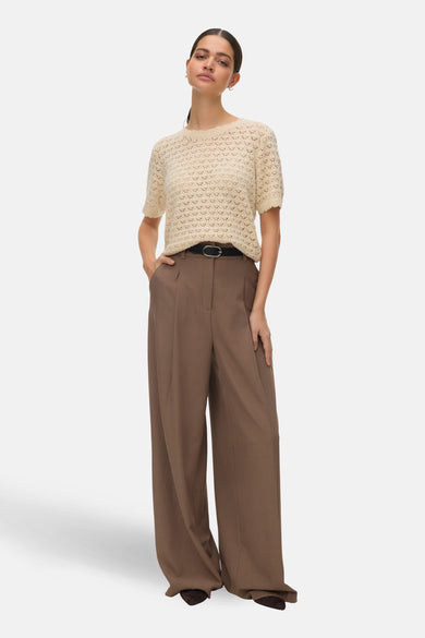 T-shirt beige à manches courtes de VERO MODA, en maille ajourée, porté avec un pantalon marron taille haute.
